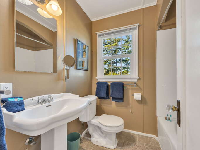 Freshen up in your bright, private bathroom, where natural light streams through a charming window overlooking lush greenery. Soft towels and thoughtful touches await your arrival.