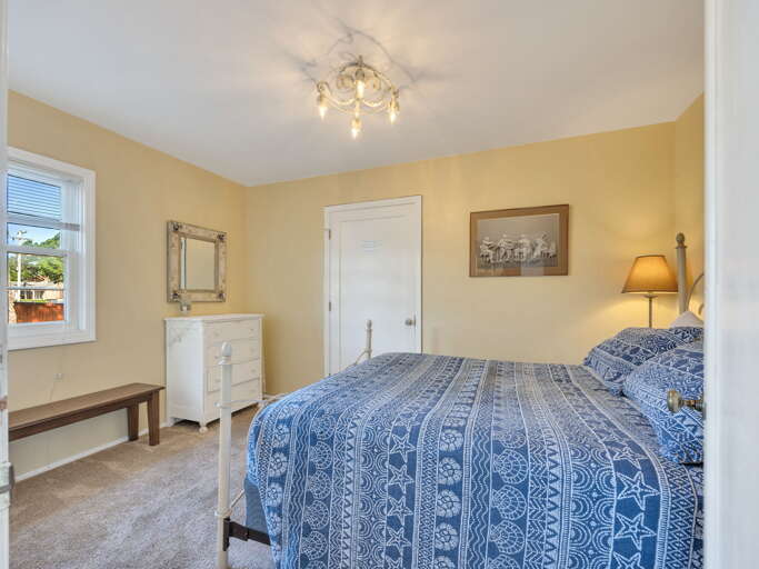 Your peaceful bedroom features soft lighting and a cozy bed dressed in cheerful blue-patterned linens. Rest easy in this sun-filled space with thoughtful touches like the vintage dresser and gentle coastal decor.