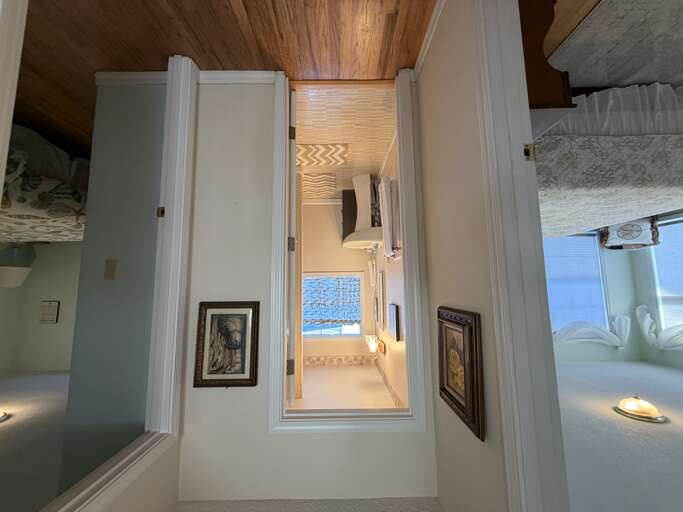 Warm wood-paneled ceilings contrast beautifully with crisp white columns, creating an inviting journey through the space. Soft lighting and artistic touches add character, guiding you from cozy living areas to a peaceful bath retreat.