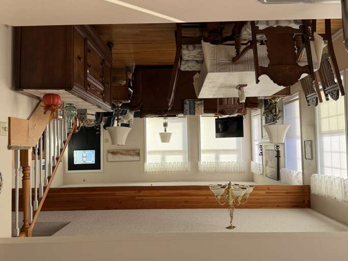 Step into a welcoming living space filled with warm wood tones and classic charm. Sunlight streams through lace-curtained windows, illuminating cozy seating and thoughtful touches that make you feel right at home.