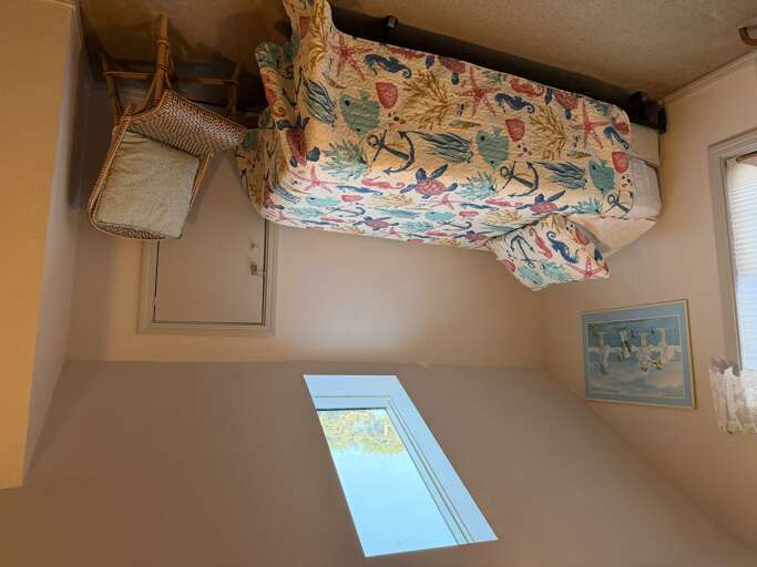 Your cozy bedroom features vibrant nautical-themed bedding and warm golden walls. A woven chair and framed artwork add charming coastal touches to your restful retreat.