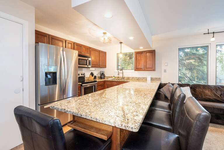 Spacious Kitchen With Sleek Surfaces In Vacation Rental, Viewed Between Plush Seating And Sunlit Windows
