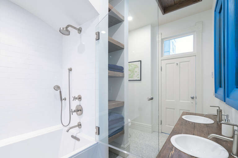 Bathroom with glass-doored shower, double vanity sinks, and shelves built into the walls.