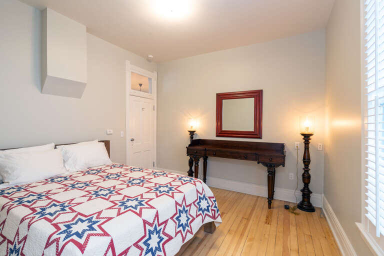 Colorful sheets on a large bed in the bedroom, by a side table and mirror.