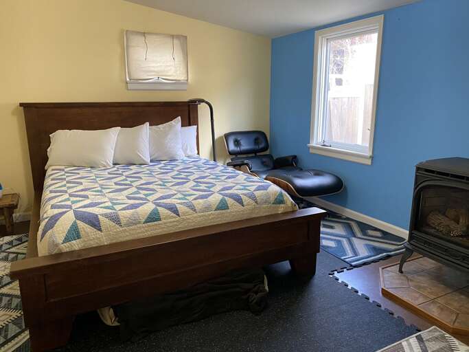 A long leather lounge stretches out beside the bed of a bedroom, complete with a old fashioned wood stove.