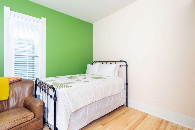 A small bed by a green wall, with a leather armchair at the foot of it.