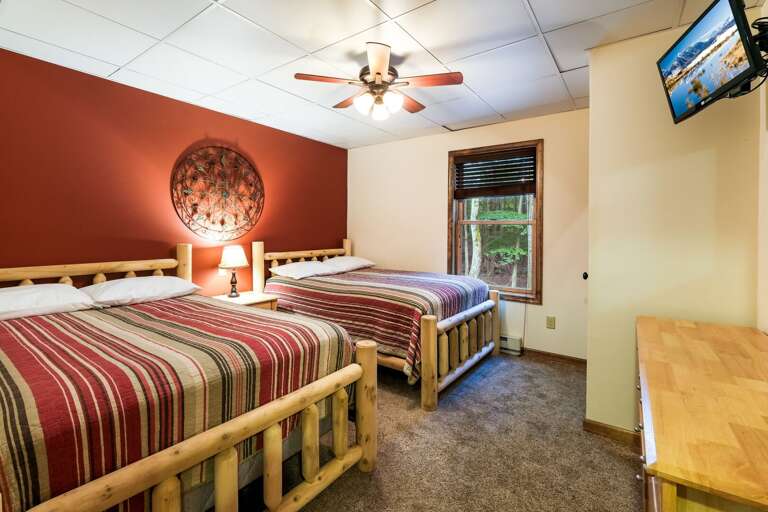 Angled photo of two beds, a nightstand and lamp, a dresser, and a TV in a bedroom.