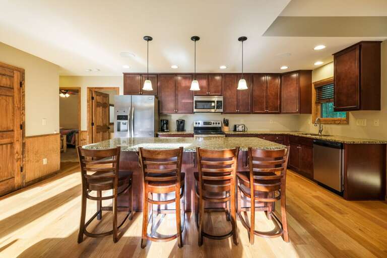 The bar seating alongside the kitchen island counter, facing the oven, microwave, and refrigerator.