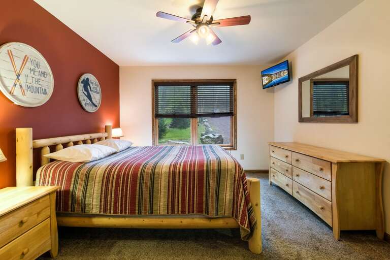 A dresser, mirror, and TV are along the right wall, a bed and nightstand on the other.