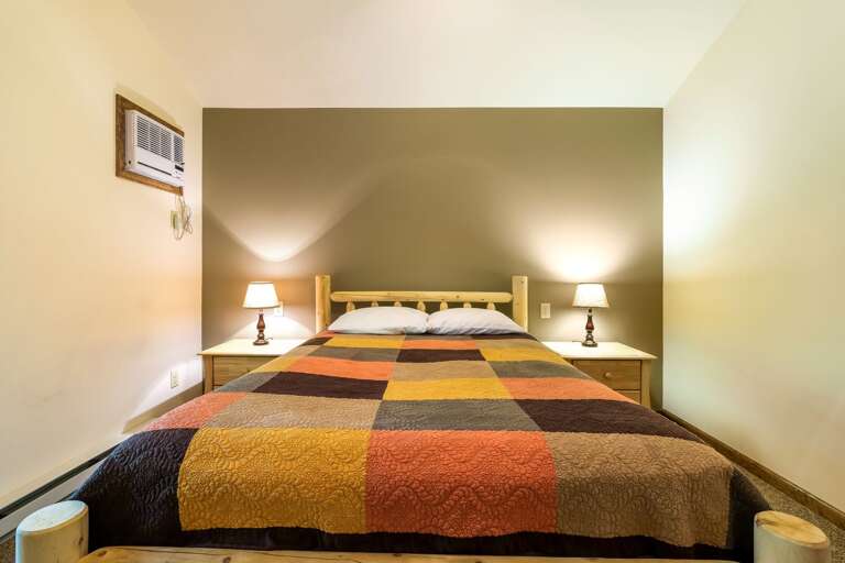 Large bed with two nightstands and lamps on either side. Air conditioner visible to left.