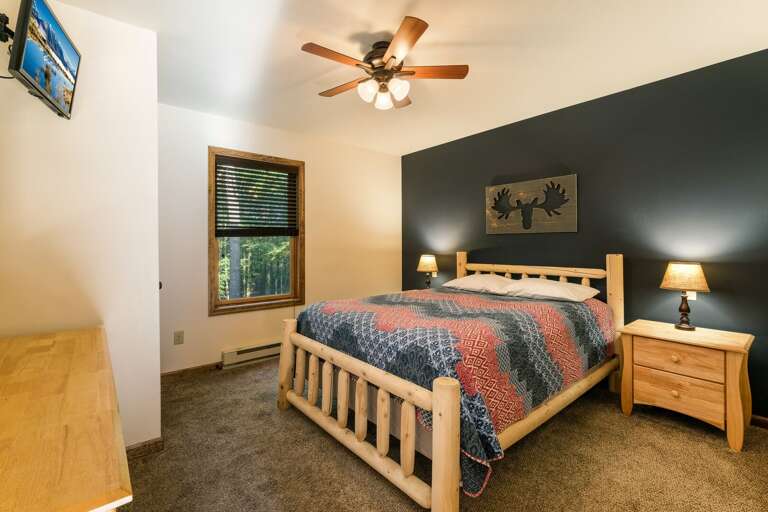 A moose painting hangs over a large bed in the center of the room, with nightstands on either side, and a dresser and TV at the foot of the bed.