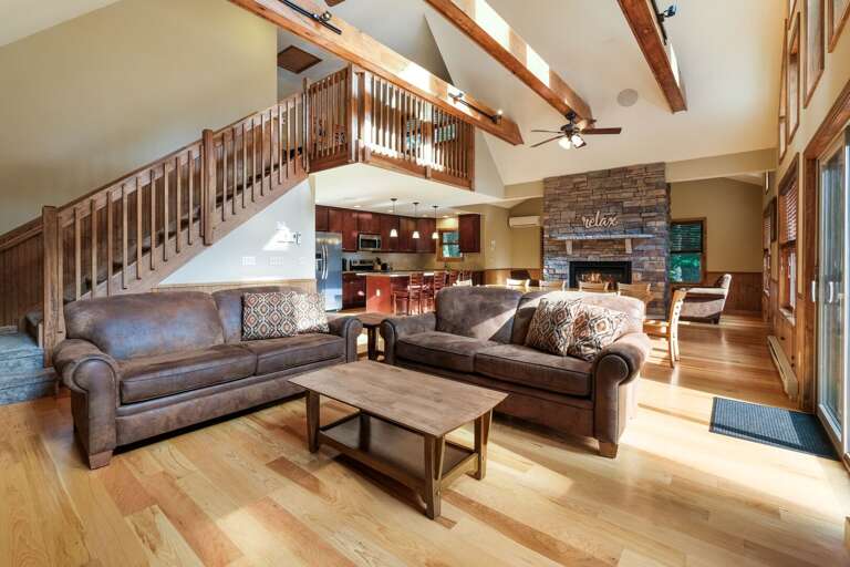 Picture of great room taken in front of fireplace, showing two couches, coffee table, and the kitchen (in the background).