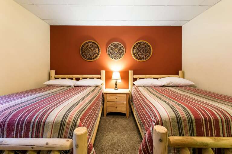 Three wall decorations hanging over a nightstand lamp and two beds in one of the bedrooms of this luxurious Poconos vacation rental.
