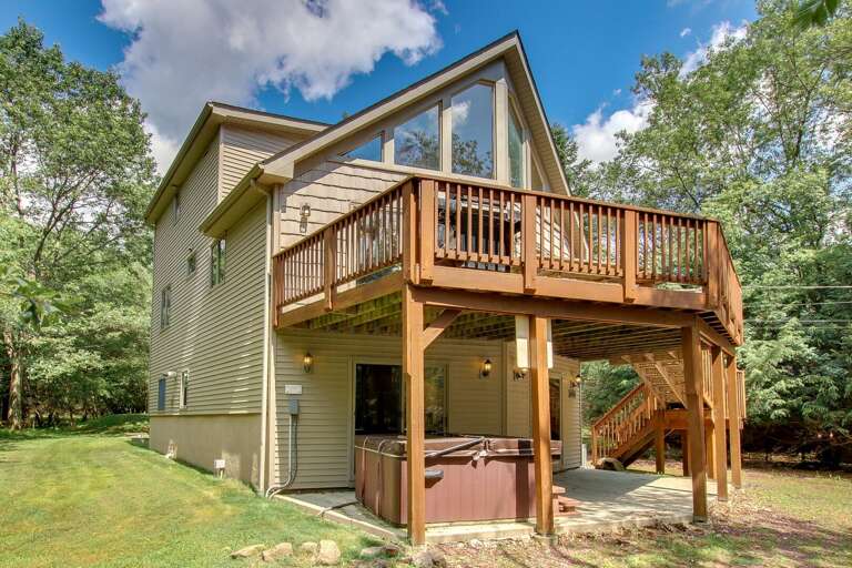 An angled picture of the exterior of this Pocono rental in Towamensing Trails, with the second floor porch and hot tub in shot.