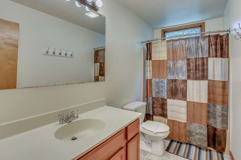 The bathroom, with toilet, sink, mirror, and shower (with curtains closed).