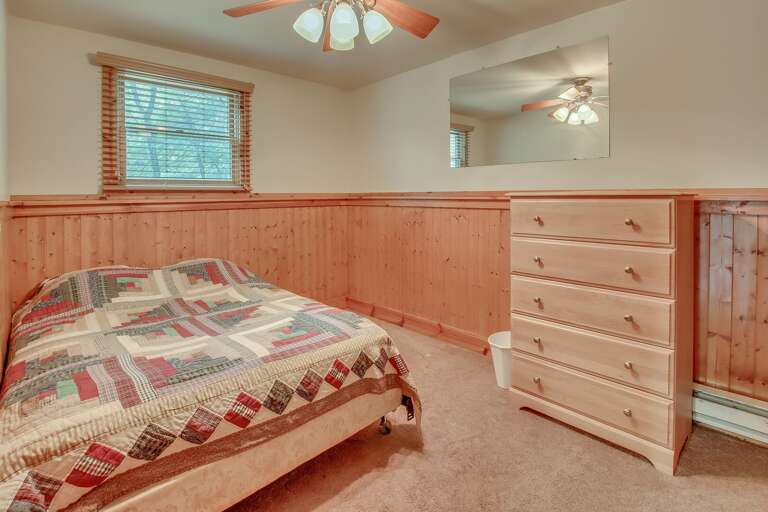 Picture of a bedroom with a quilt covered bed, dresser, and mirror on the wall.