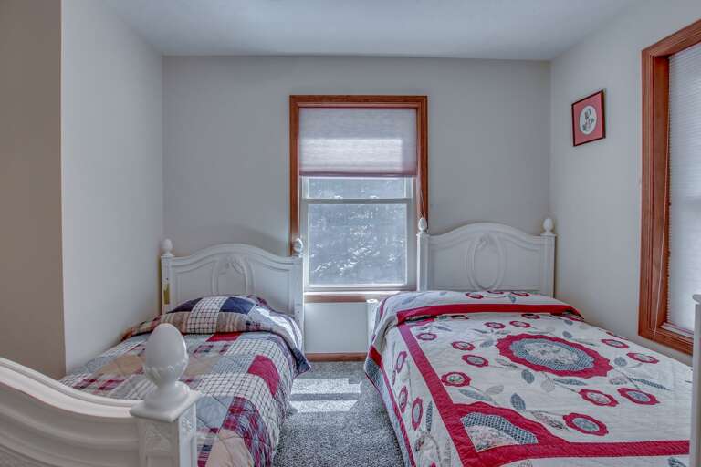 A picture taken from the foot of two beds next to one another, with a window between them. A picture taken from the foot of two beds next to one another, with a window between them.