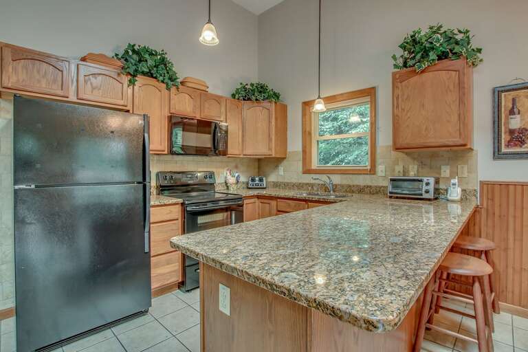 Picture of the kitchen with the refrigerator, oven, microwave, and island with chairs in shot. Picture of the kitchen with the refrigerator, oven, microwave, and island with chairs in shot.