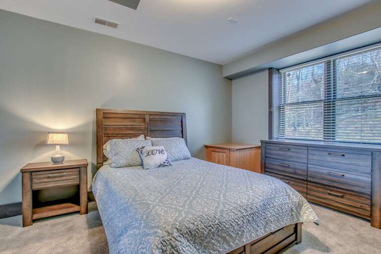 Angled picture of a large bed, nightstand with lamp, and large dresser.