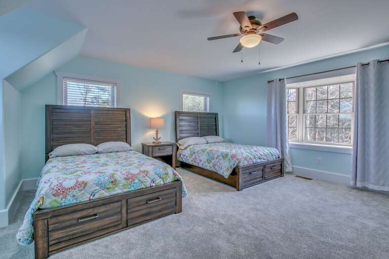 Two beds side by side in one of the bedrooms of this Poconos rental  by the lake, with a nightstand in between.