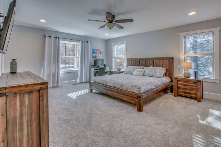 Master bedroom of this Poconos rental by the lake, with large bed, nightstand, computer desk, and a TV and dresser in front of the foot of the bed.