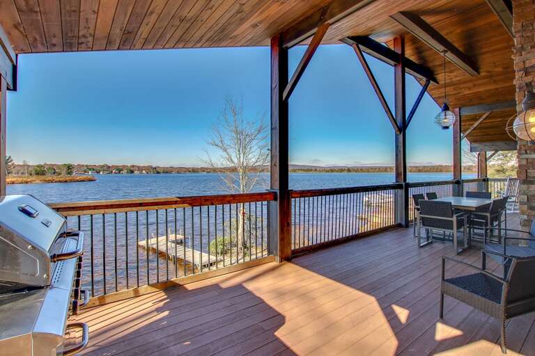 A view out onto the lake from the back porch of this Poconos rental by the lake, with porch table and chairs, and a grill to the left.