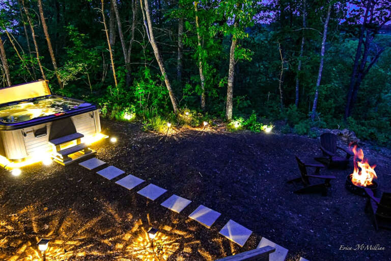 Forest Fireside With Furnished Path Leading To Lit Jacuzzi Under Twilight Trees