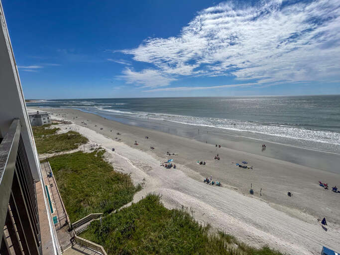 Seaside View With Sandy Shore, Scattered Sunbathers, And Surging Waves