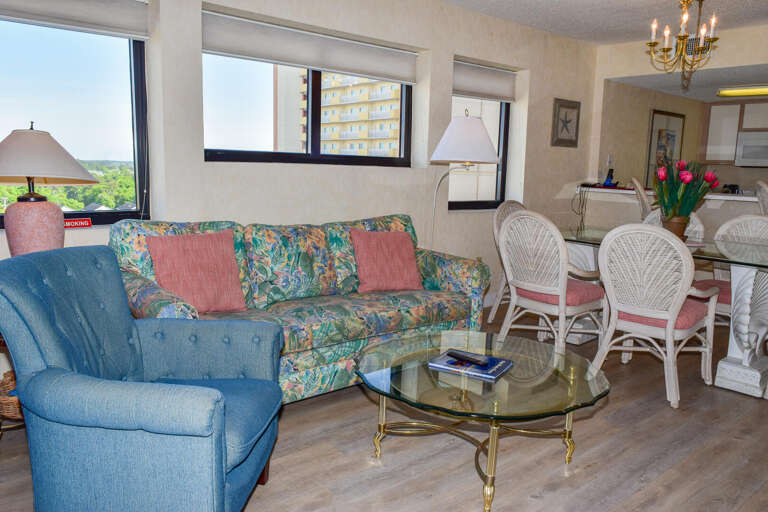Polished Living Space In Vacation Rental With Floral Sofa, Blue Chair, And Glass-top Table