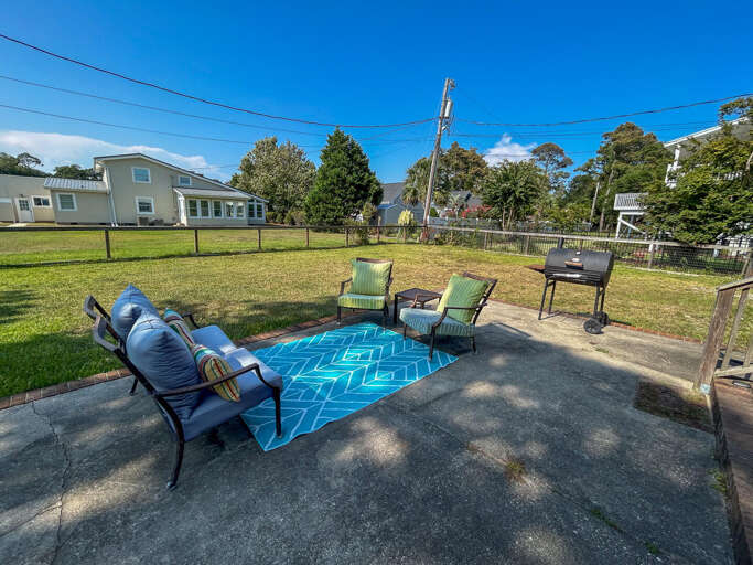 Backyard Barbecue Beneath Blue Skies, Chairs On Concrete, Grass Greenery Around
