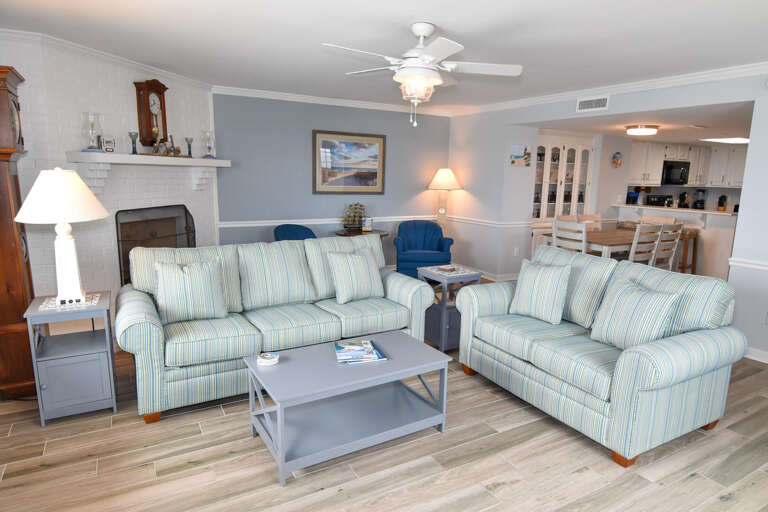 Living Area With Light Blue Sofas, Pale Walls, Wooden Floors, And A Central Coffee Table