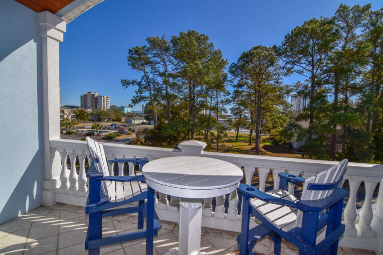 Bright Balcony View With Blue Chairs And White Table Overlooking Pine Trees And Cityscape