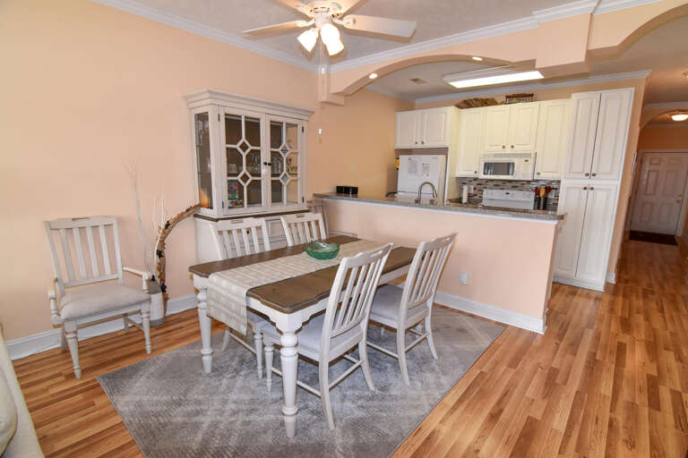 Pale Walls With Wooden Floors, White Kitchen; Chairs Surround A Dining Table