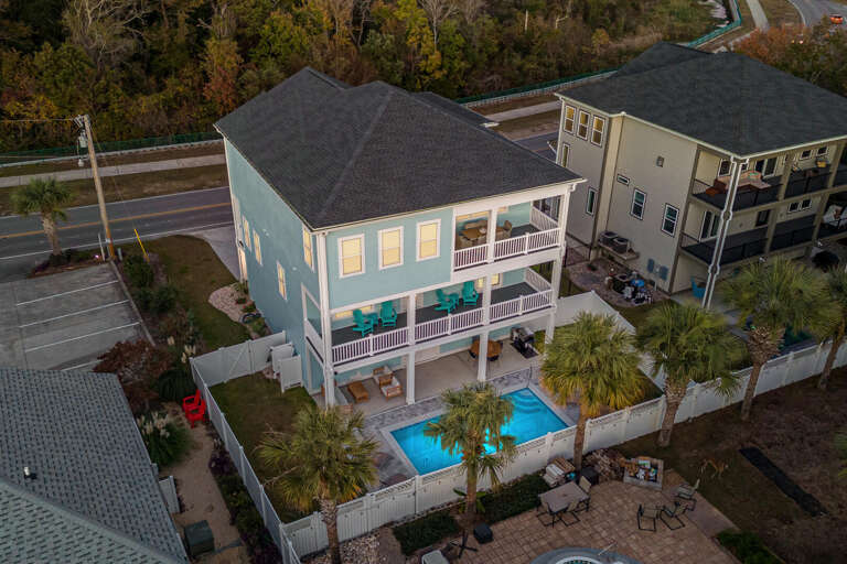 Aerial View Of A Pale Blue Building With A Pool, Trees, And Evening Shadows