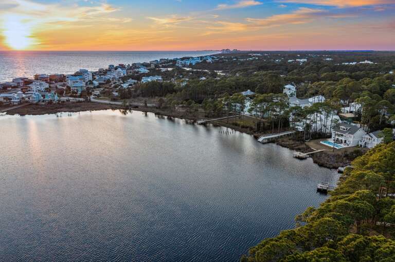 Aerial View Of A Waterfront Residential Area At Sunset With Serene Lake And Lush Landscape
