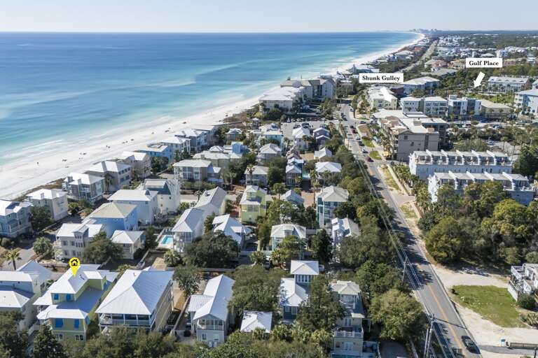 Aerial View Of Vibrant Vacation Rentals Lining A Lush Lane Near A Serene Sea Strand