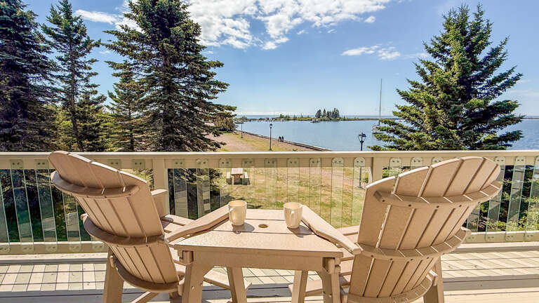 Two Adirondack chairs on your private balcony overlook towering pines, a peaceful harbor, and sweeping waterfront vistasâthe perfect spot for morning coffee.
