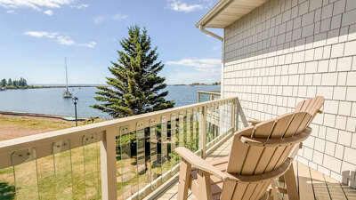 Unwind in your own waterfront sanctuaryâtwo Adirondack chairs await on a private balcony overlooking serene waters, sailboats drifting by, and lush greenery stretching to the horizon.