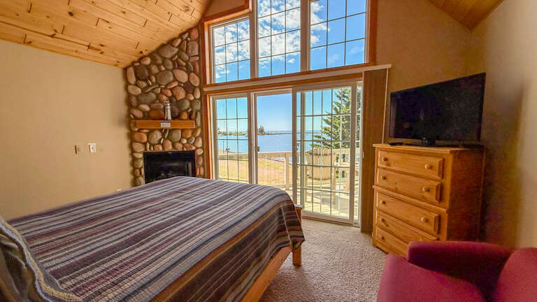 Wake up to stunning lake views through floor-to-ceiling windows, with a cozy stone fireplace adding mountain charm to your peaceful retreat.