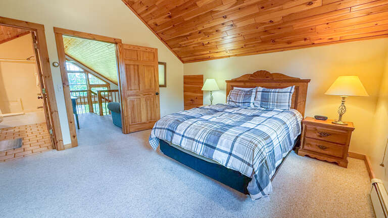 Your cozy bedroom features a plush bed with crisp plaid linens, warm wood furnishings, and a private en-suite bathroom just steps away for your convenience.