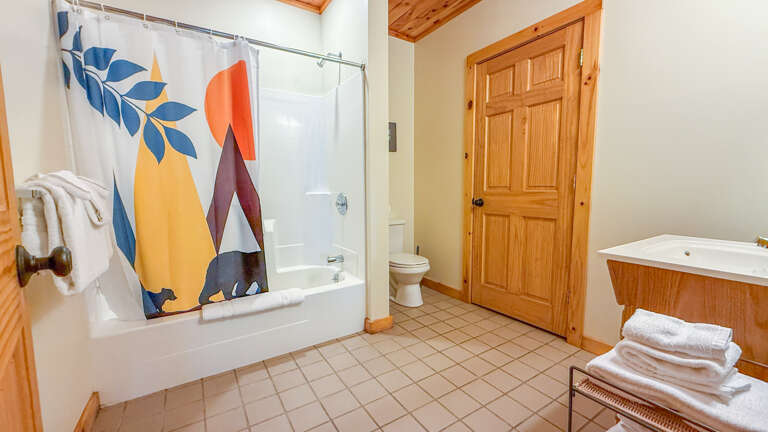 Your private bathroom features a full tub-shower combo, fresh towels, and charming mountain-themed décor—everything you need to refresh after a day of adventure.