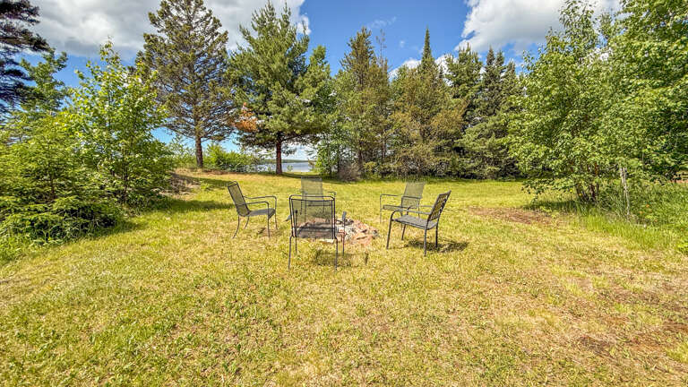 An open grassy area surrounded by mature trees with seating arranged around a central fire pit, perfect for relaxing in a natural setting.