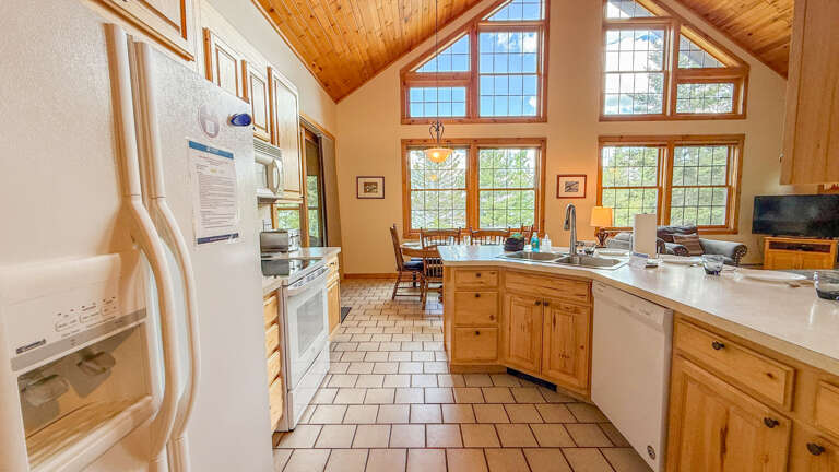 Your fully equipped kitchen welcomes gatherings under vaulted wood ceilings with sunlight streaming through tall windows, ideal for preparing meals together while surrounded by the warmth of natural light.