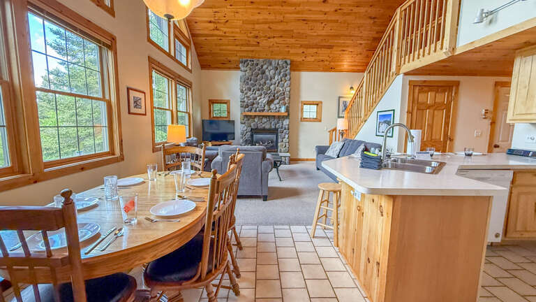 Picture yourself here: natural light streams through oversized windows, filling this open-concept retreat with warmth. A grand stone fireplace anchors your living space, while the fully equipped kitchen and cozy dining area set the stage for memorable mea