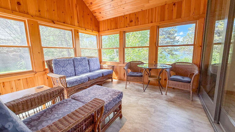 Sink into plush wicker seating as natural light floods through panoramic windows, framing peaceful lake views. Your perfect retreat for morning coffee or sunset relaxation.