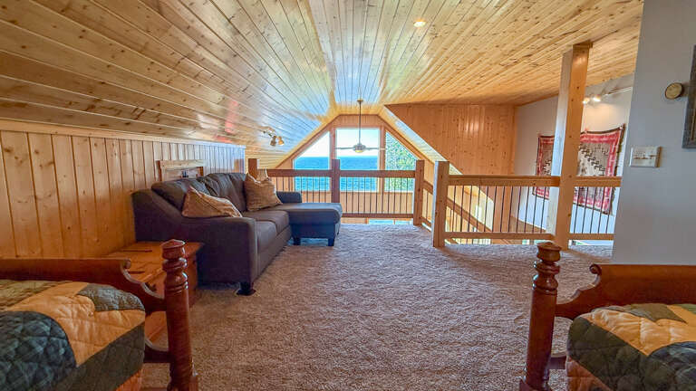 Your private loft retreat with stunning lake views through the vaulted windows—curl up on the plush sectional or relax on twin beds, all while soaking in the peaceful waterfront scenery.