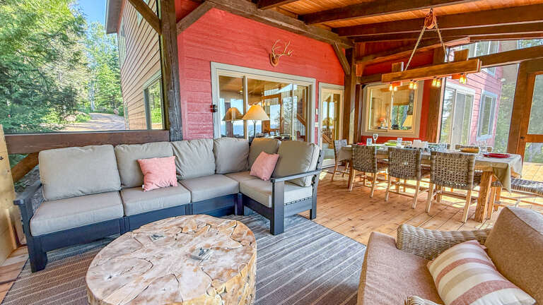 Unwind in your private covered patio, where rustic wood beams frame a plush sectional sofa and an inviting dining space surrounded by forest views.
