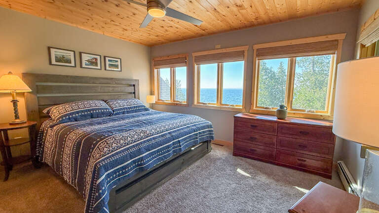 Wake up to stunning lake views framed by natural wood and warm light. Your peaceful retreat features a cozy bed, charming décor, and windows that open to the serene water beyond.