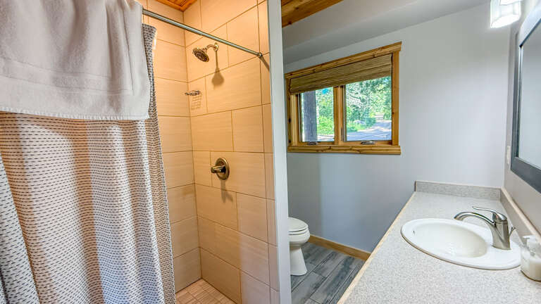 Your private bathroom features a refreshing walk-in shower with modern fixtures, natural wood accents, and a bright window bringing in forest viewsâa peaceful retreat to start your day.
