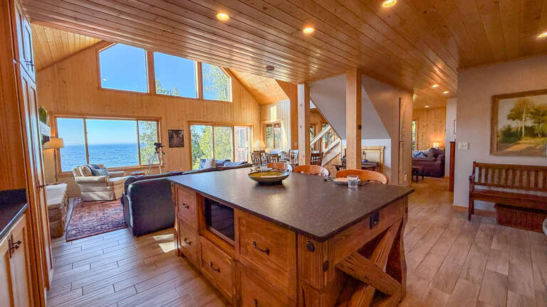 Sunlight pours through expansive windows, framing stunning water views in this open, wood-warmed retreat. The spacious kitchen island invites you to gather, cook, and linger with loved ones while soaking in coastal serenity.